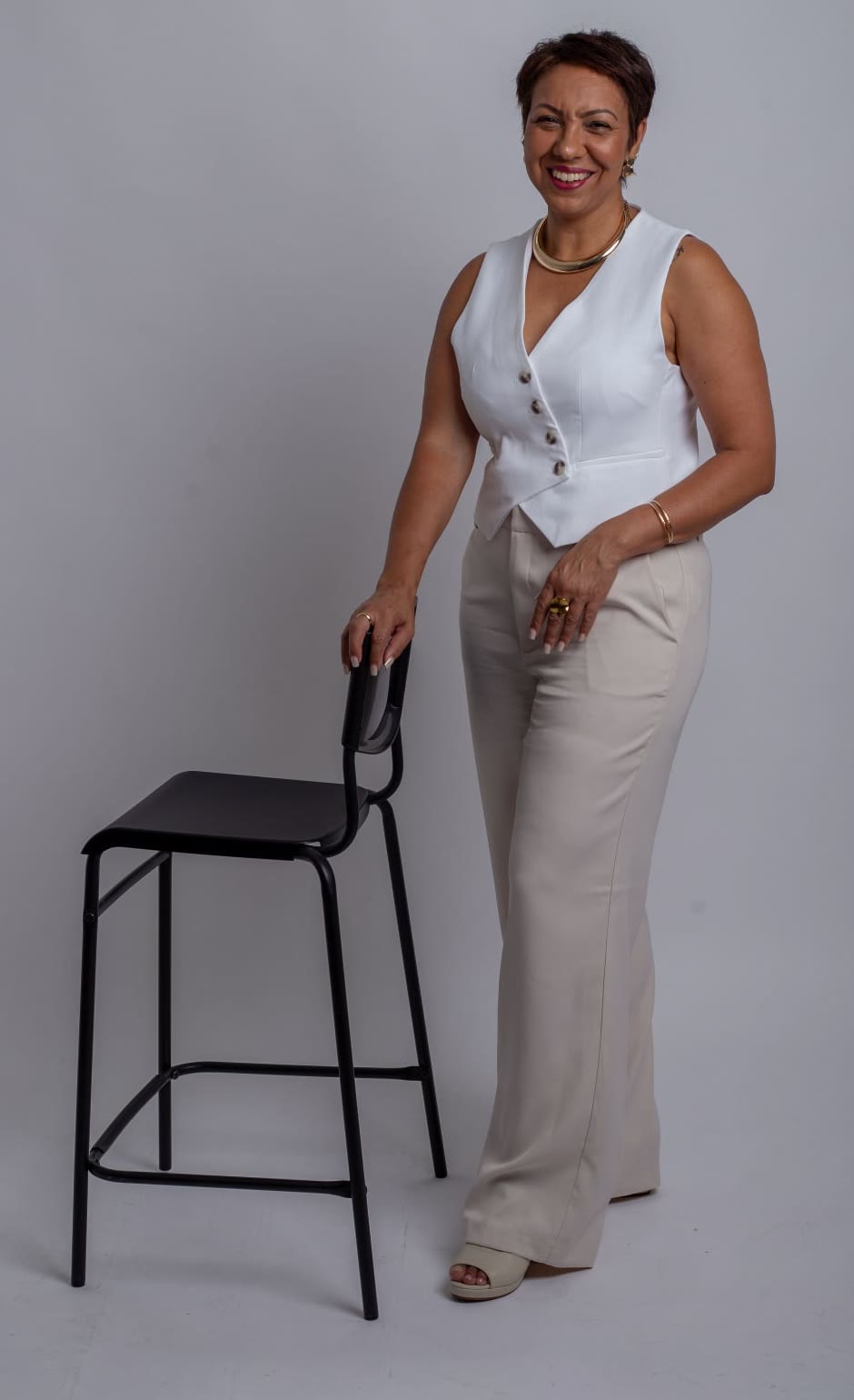 Cris Rodrigues em pé, de colete branco, apoiada numa cadeira